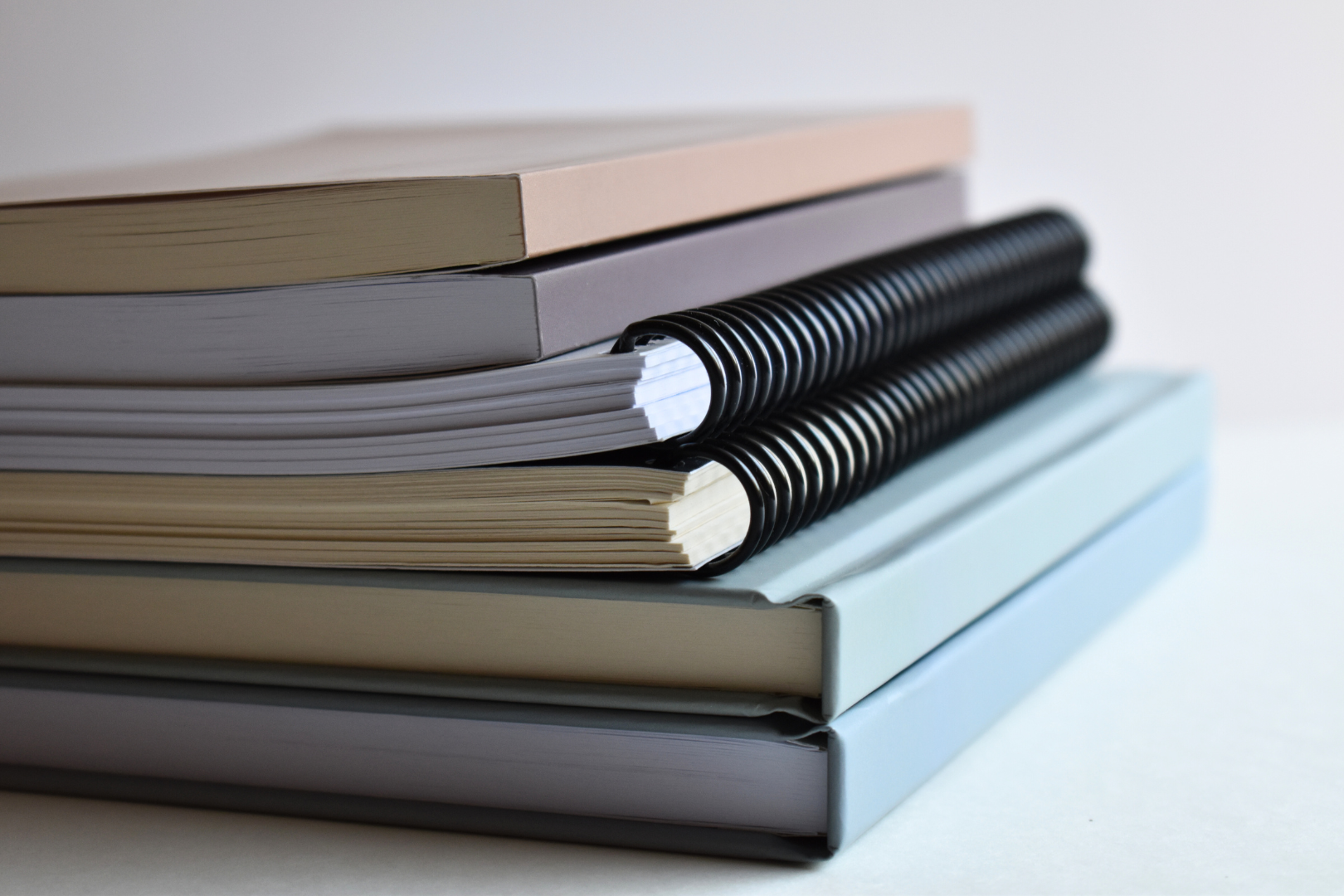 Stack of planners and journals with different cover colors and binding, including paperback, spiral or coil, and hardcover
